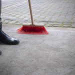 Un piéton en bottes à côté d'un balai rouge sur béton