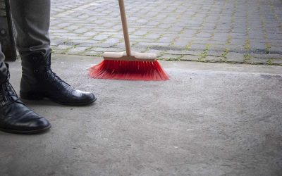 Un piéton en bottes à côté d'un balai rouge sur béton