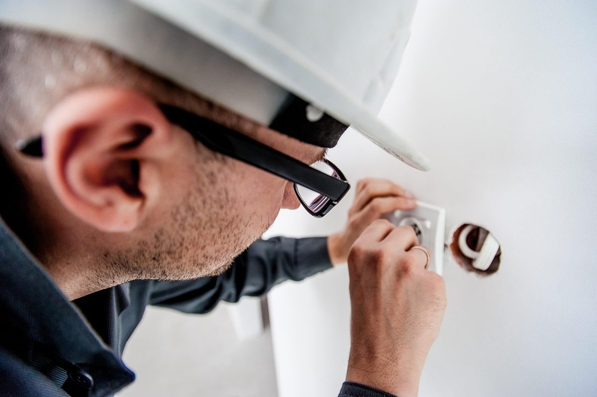 Homme en casque et lunettes manipulant un objet dans un trou de mur Homme en casque et lunettes manipulant un objet dans un trou de mur